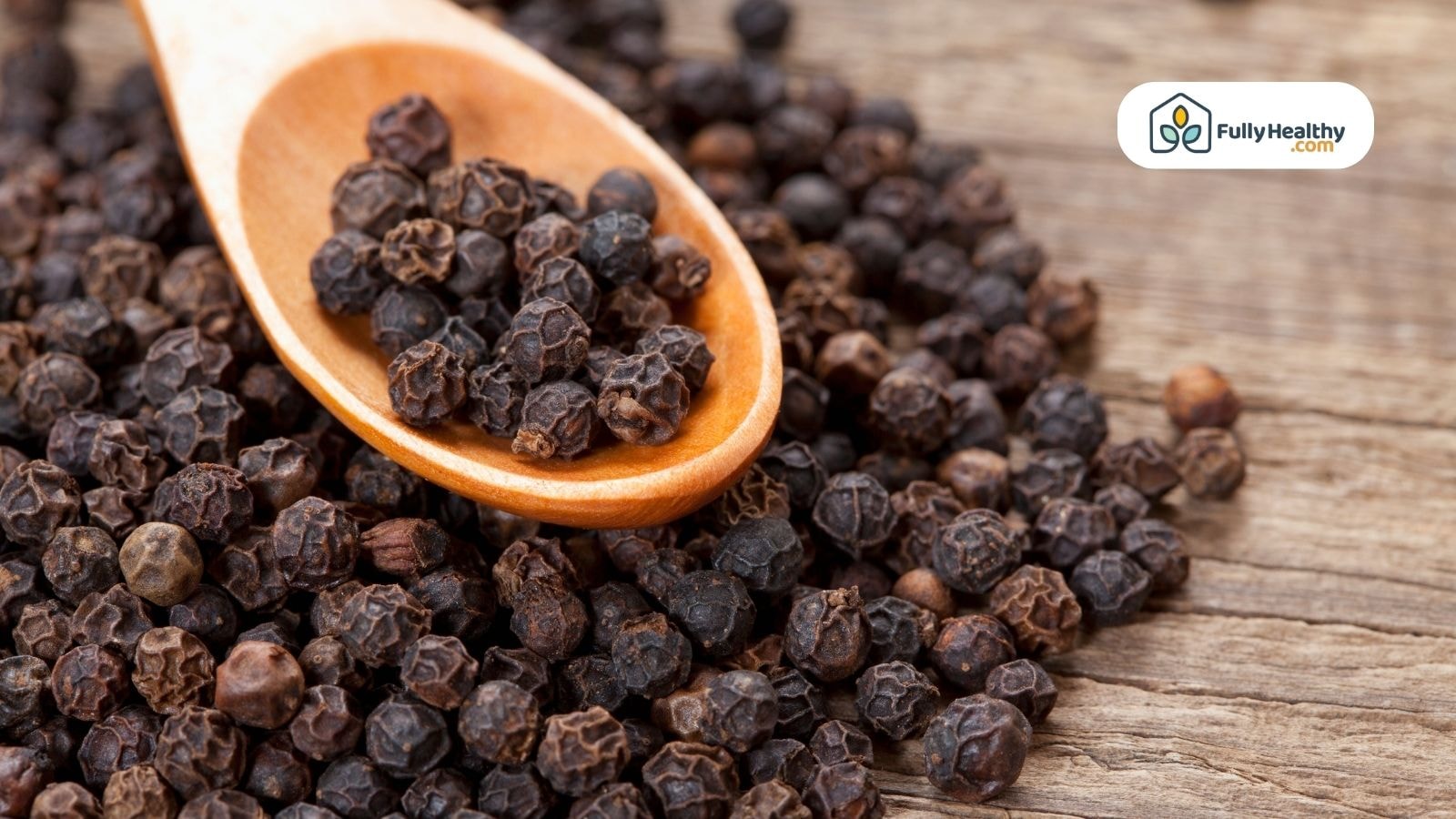 Close-up of whole black peppercorns in a wooden spoon, placed on a rustic wooden table