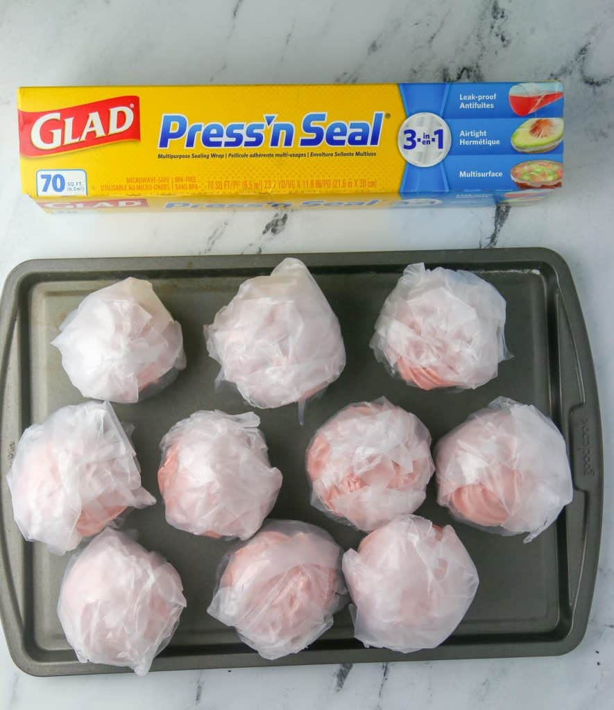 wrapped cupcakes on a baking sheet with a box of plastic wrap next to it