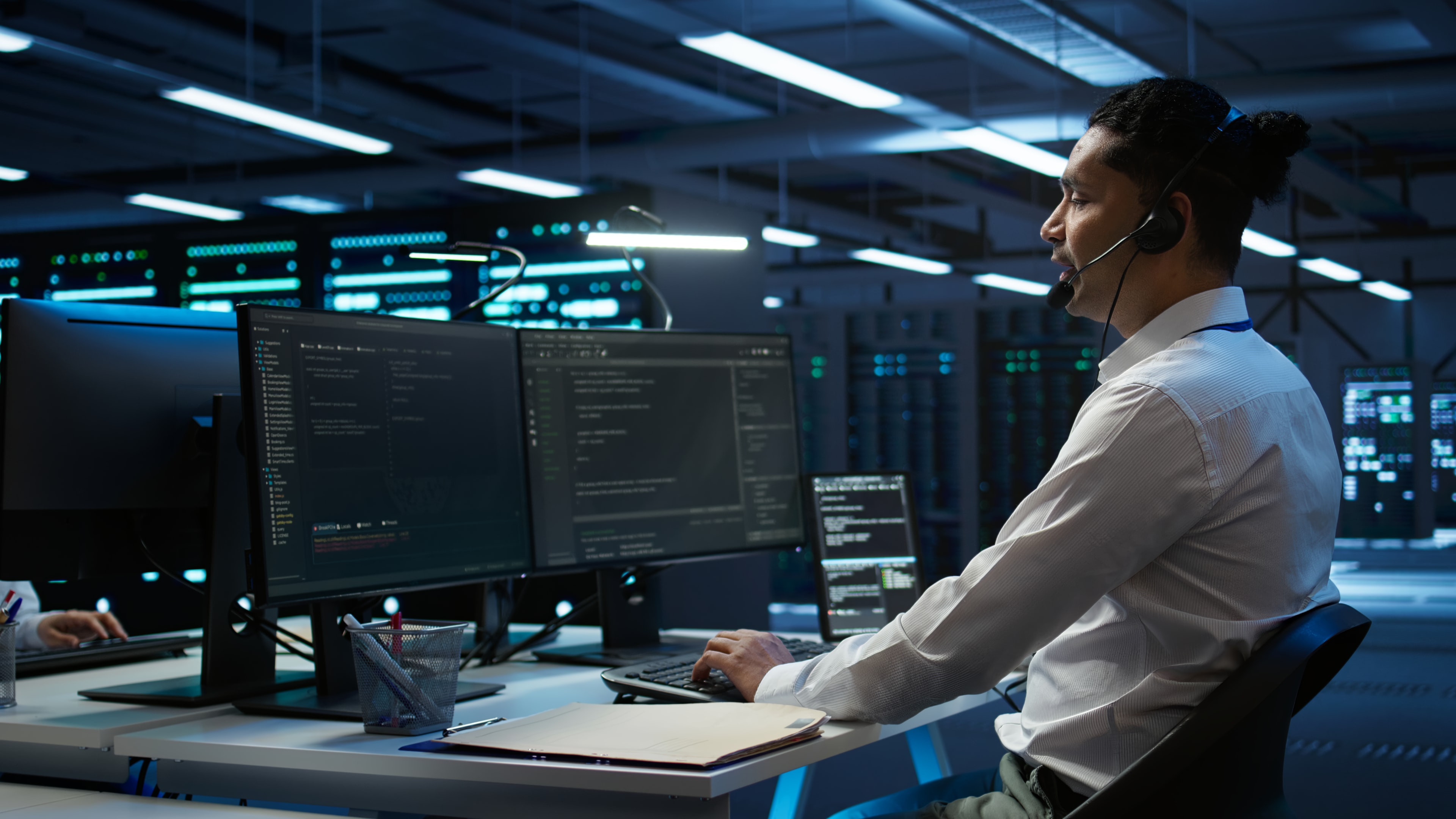 IT professional wearing a headset seated at a desk with multiple monitors in a data center, providing real-time support and monitoring as part of managed IT services from a proactive managed IT service provider.