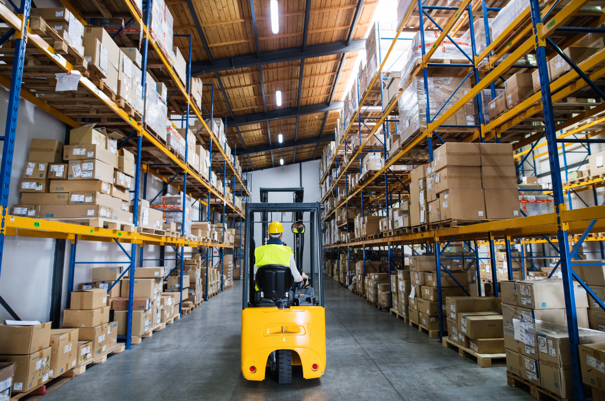 Warehouse worker driving forklift truck down factory aisle.