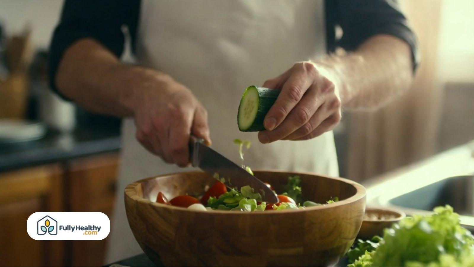 Person preparing cucumbers in a fresh salad with vegetables.