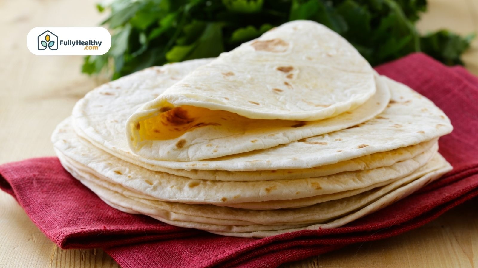 Folded flour tortillas stacked on red napkin with green garnish