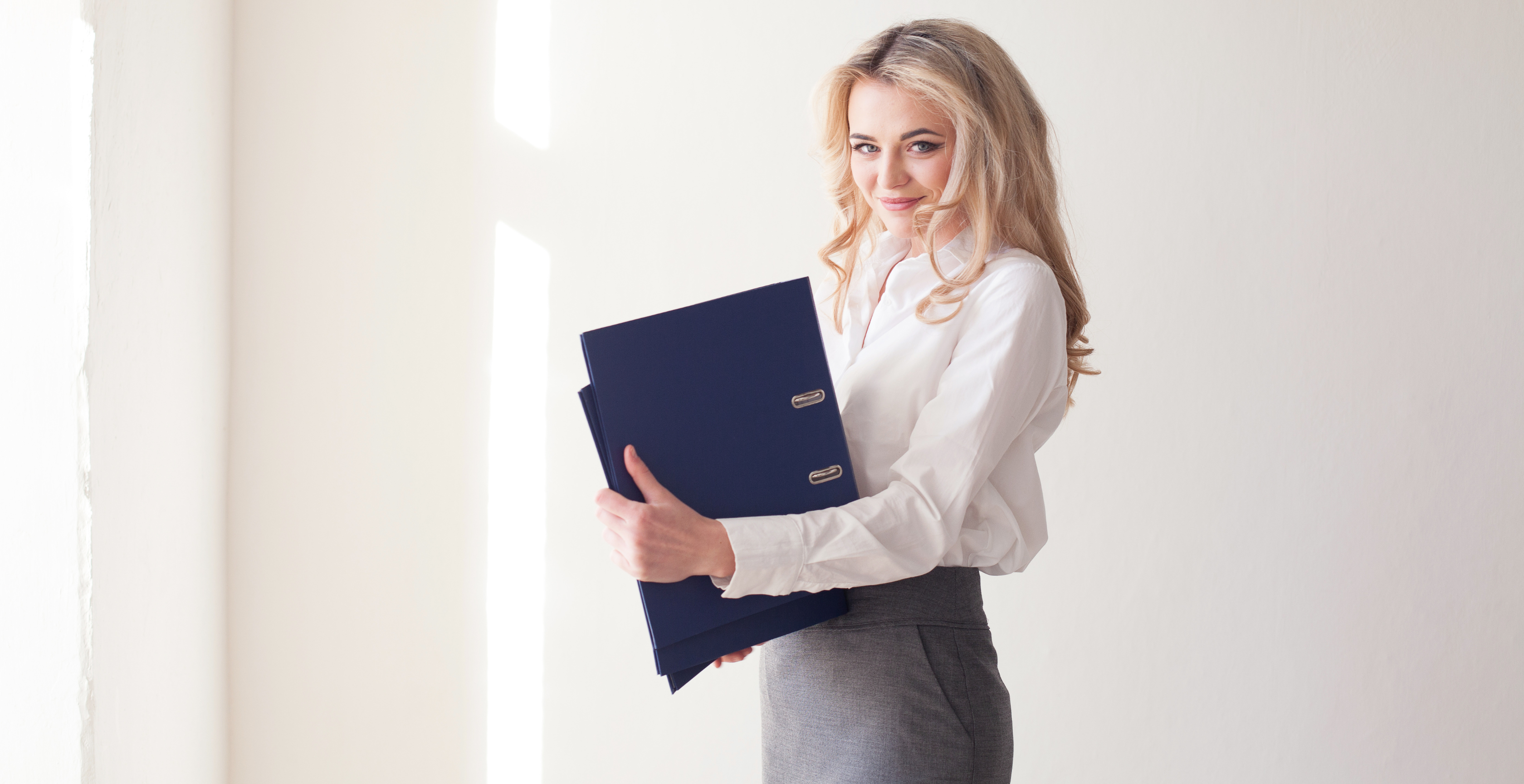 A woman in a white blouse and grey skirt holding blue binders and smiling. This image can symbolize a professional providing efficient OnlyFans bookkeeping services.