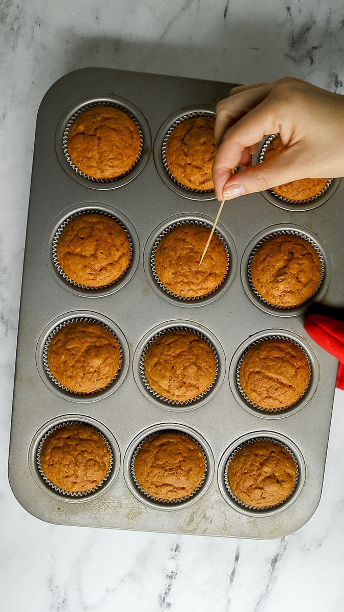 toothpick testing a baked pumpkin cupcake in the pan