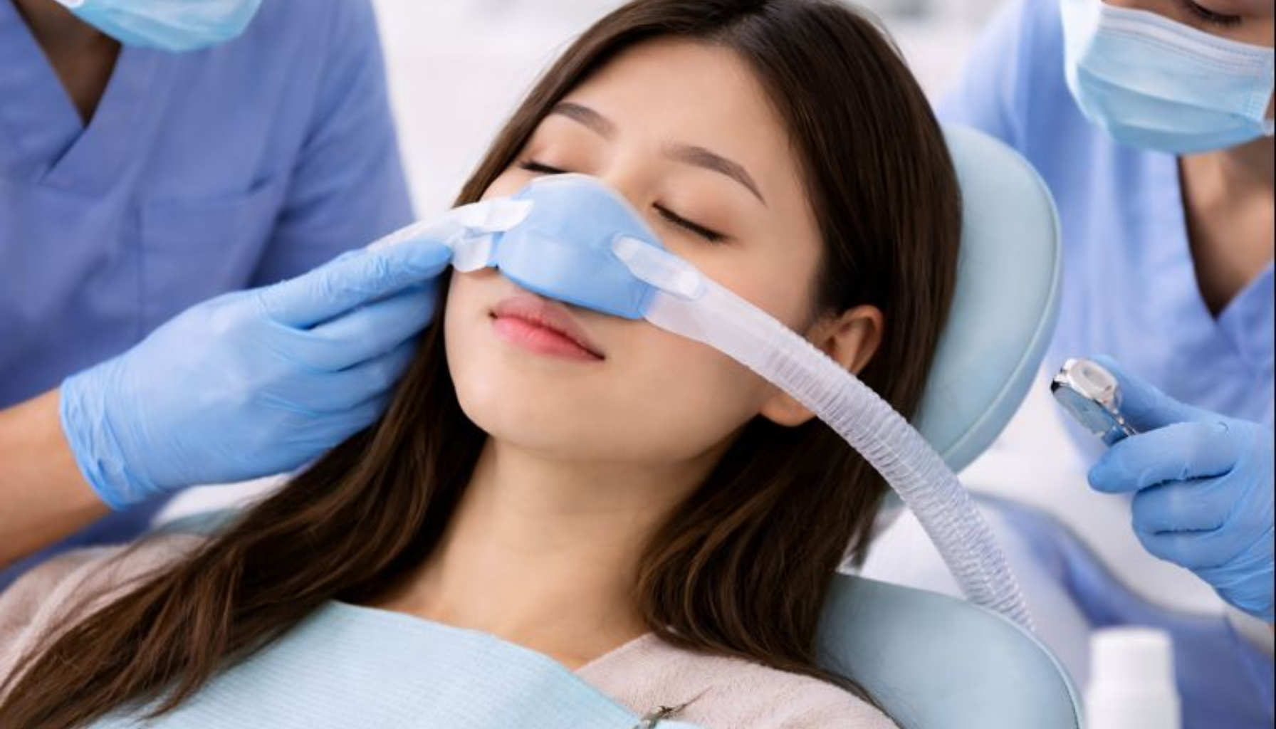 Sedasjon hos Tannlegen: En Trygg Løsning for Engstelige Pasienter 12 Kvinne mottar trygg sedasjon hos tannlegen med nesemaske, omgitt av helsepersonell i rolige omgivelser.