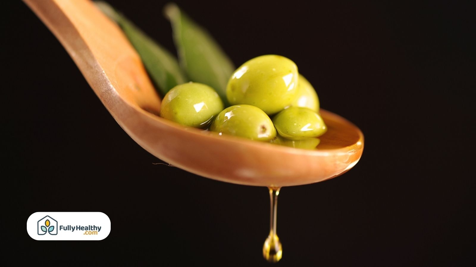 Green olives resting in a wooden spoon with a drop of olive oil dripping down, dark background.