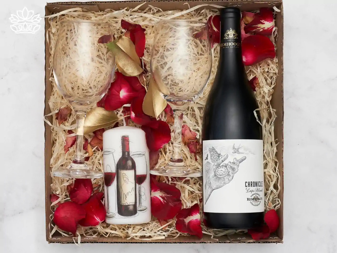 Elegant Secretary's Day gift box containing a bottle of fine wine, a decorative wine glass, and a candle, nestled among red rose petals and gold leaves, perfect for a sophisticated celebration. Fabulous Flowers and Gifts.