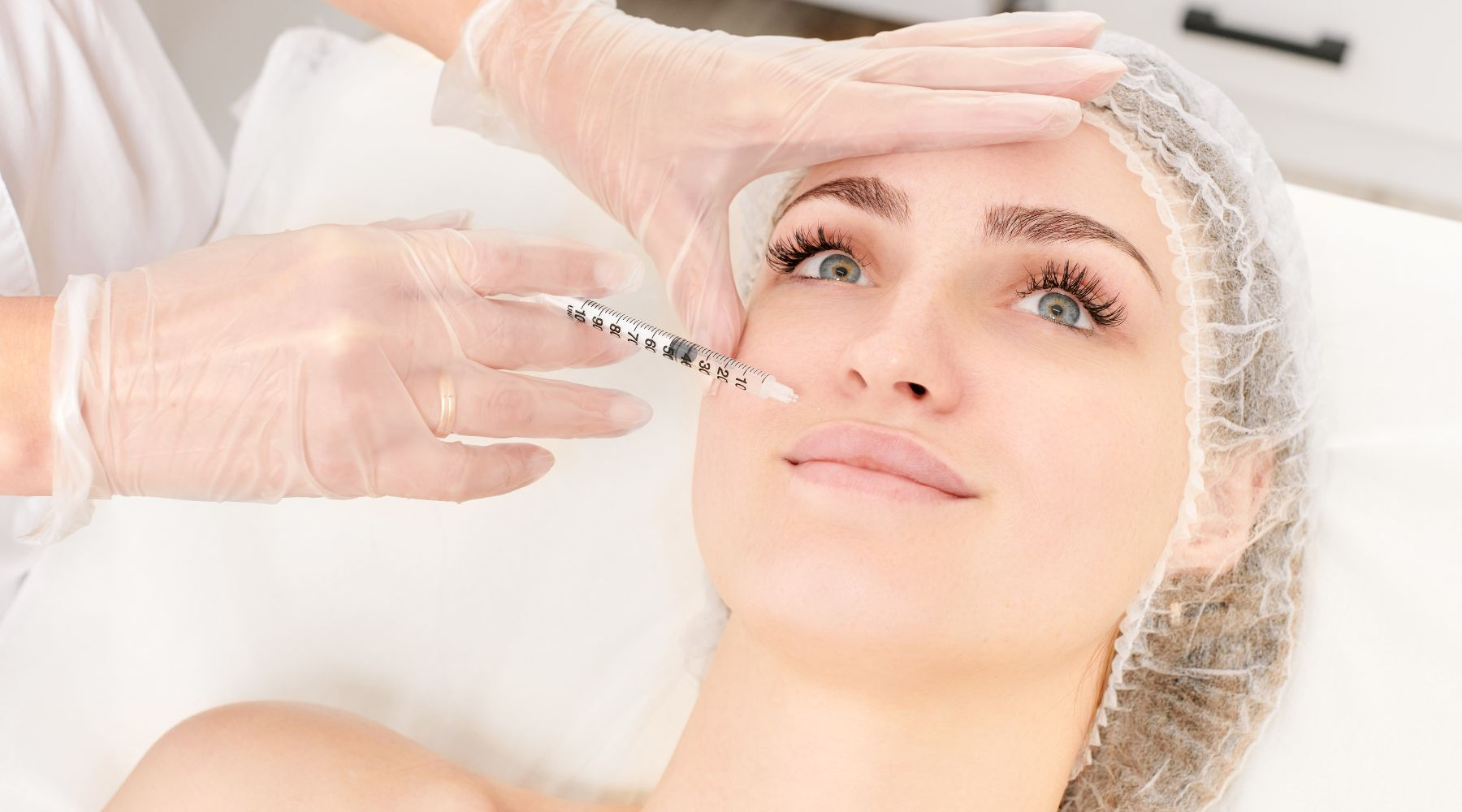 Cosmetic professional applying a syringe near the eye area of a woman during a botox treatment session