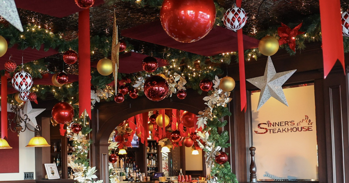A richly decorated Christmas pop-up bar inside Sinner’s Steakhouse featuring hanging ornaments, garland, gold and red holiday balls, stars, ribbons, and glowing lights that transform the space into a festive winter wonderland.