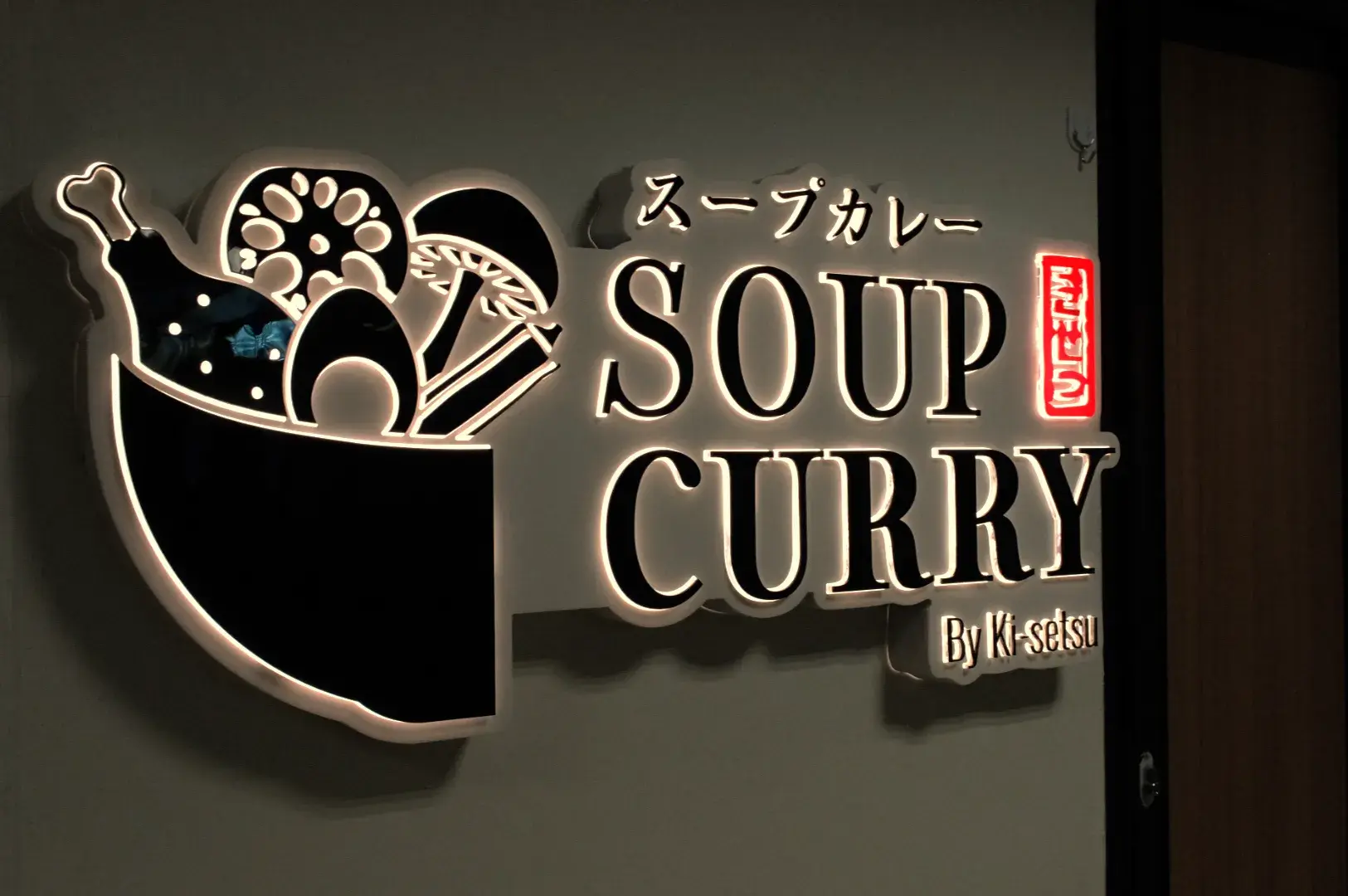 A sign that says "SOUP CURRY" with Japanese text above it, featuring graphics of food items like vegetables and meat.