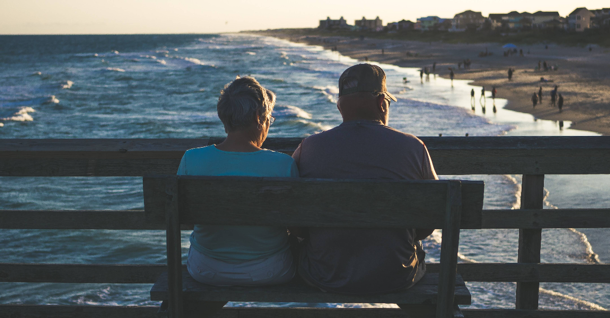 Een man en een vrouw zitten op een bankje en kijken uit naar de zee. 