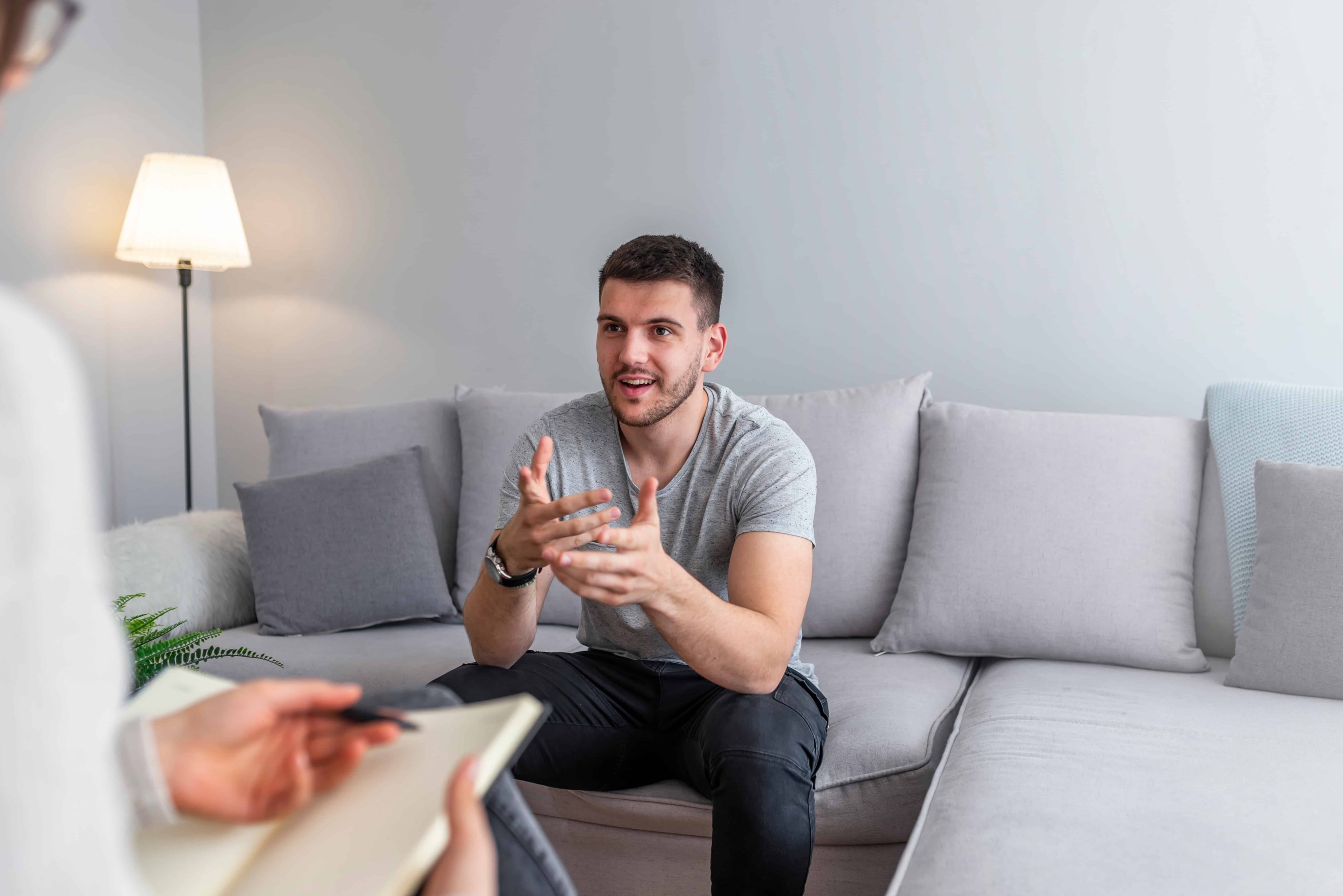 A man using the powerful tool of therapy to get rid of the toxic people in his life. He is on a couch while wearing a grey shirt.