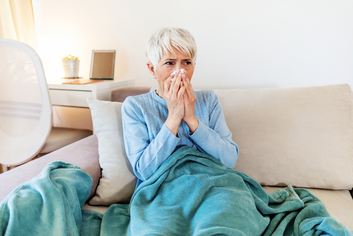 An image of a mature woman blowing her nose into a tissue. 