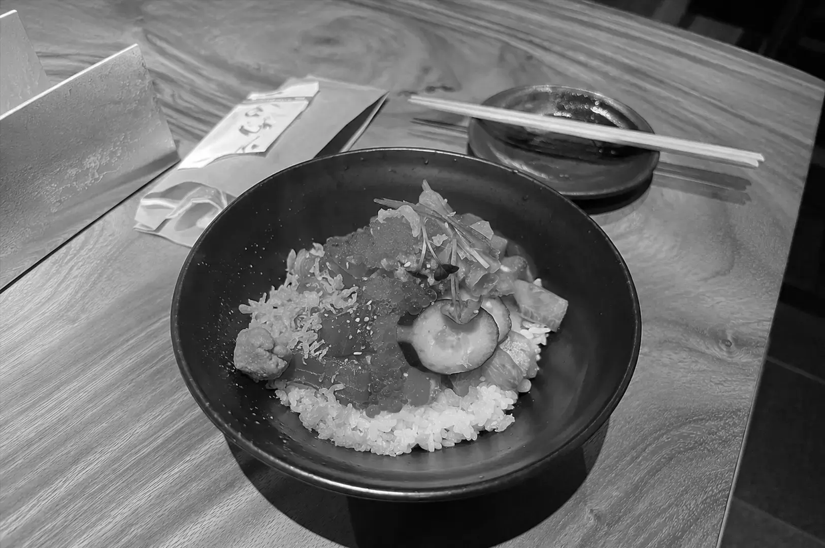 Koji Sushi Bar chirashi don with assorted sashimi, ikura, cucumber, tobiko, and Japanese rice in a black bowl.
