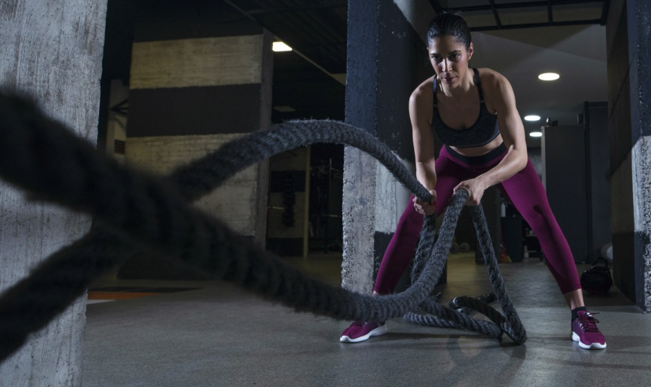 Woman performing battle rope intervals in a gym, building cardiovascular endurance and muscular endurance with full-body effort.