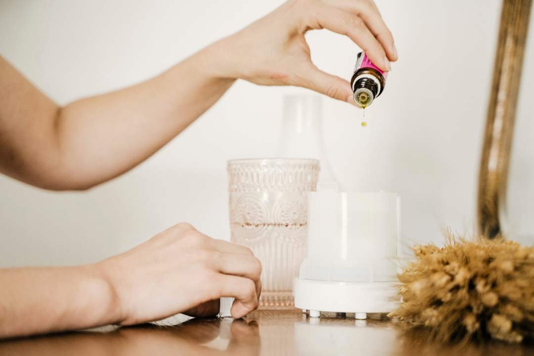 Hand pouring essential oil into a diffuser for aromatherapy, creating a calm, fragrant home environment.