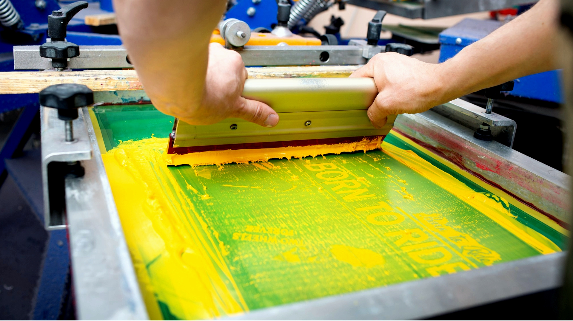 A person printing a design on a screen printing press using printing ink