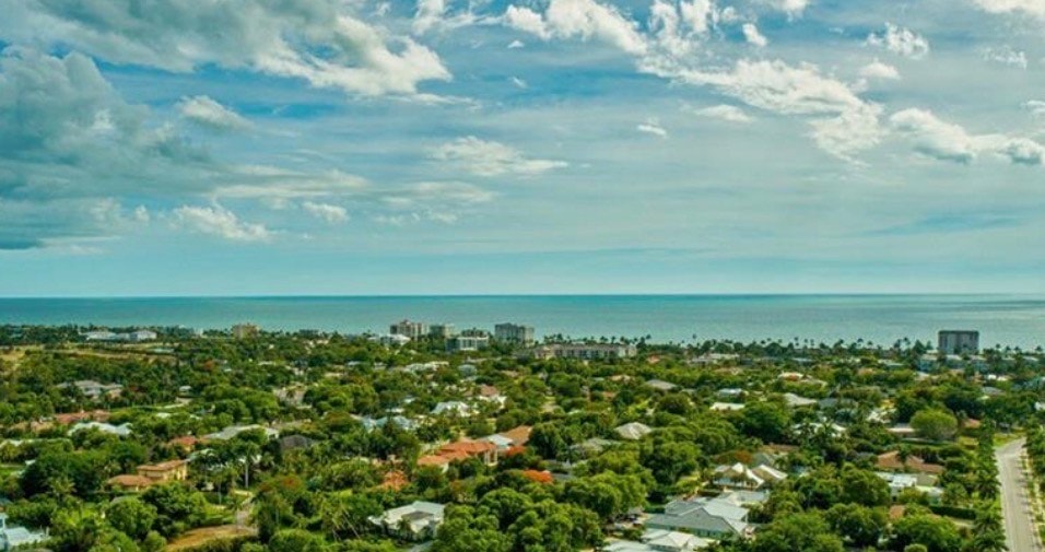 The image depicts the beautiful Lake Park neighborhood in Naples, showcasing tree-lined streets adorned with mature oak trees and luxurious homes that embody relaxed Florida living. This desirable community features stunning architecture and a serene atmosphere, perfect for those seeking a prestigious lifestyle in southwest Florida.