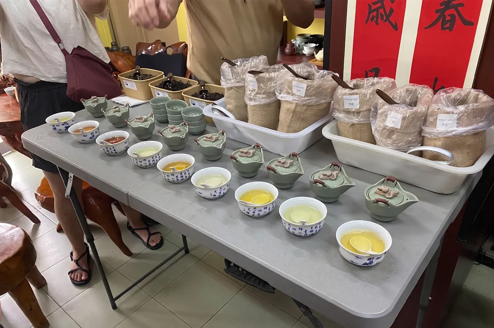 Tea cupping setup with porcelain tasting bowls, small teapots, and sacks of tea leaves.
