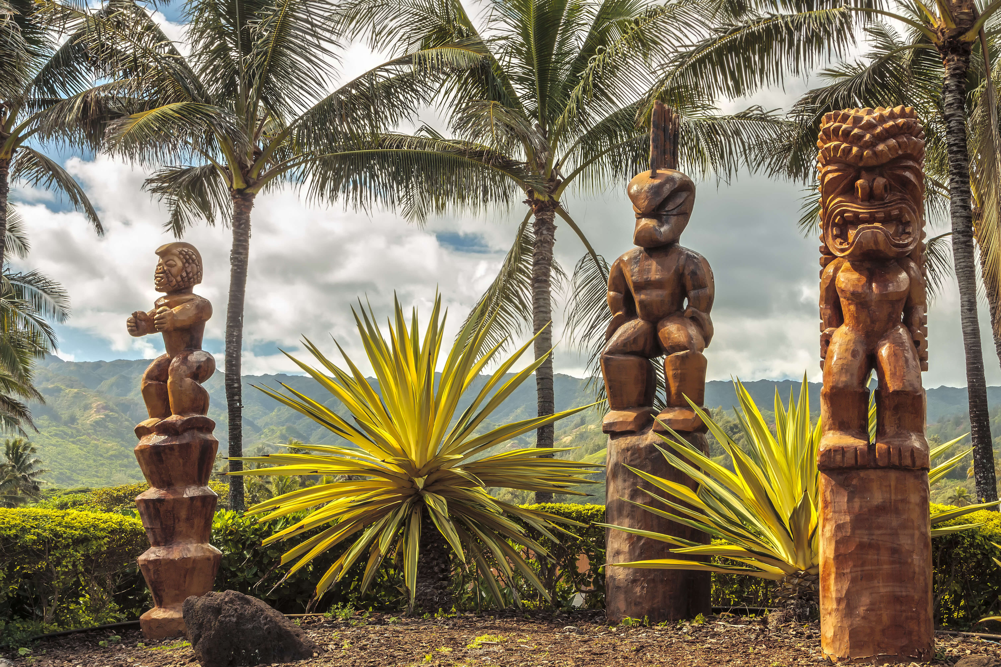three traditional Tahitian wooden carved figures on platforms with
    palm
    trees behind