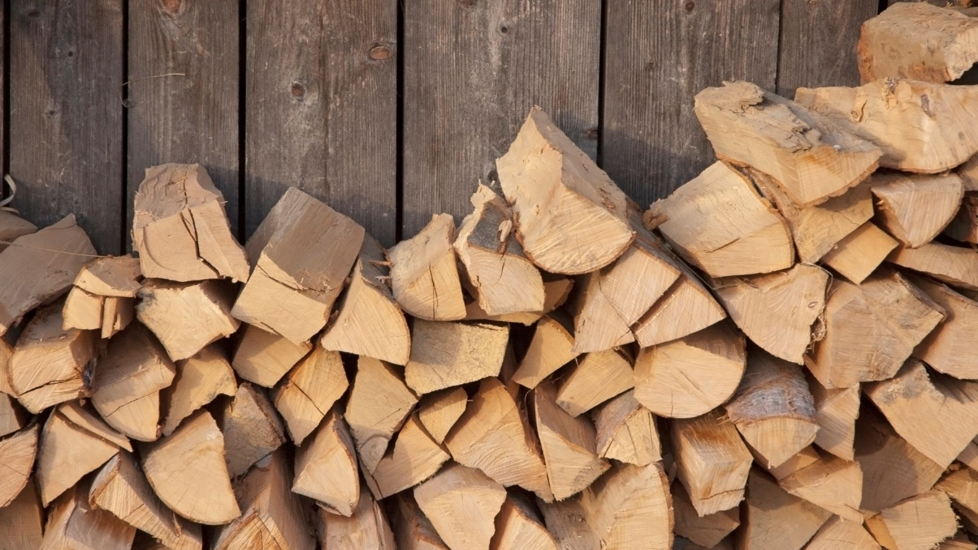 An image of cut firewood stacked alongside a wooden home.