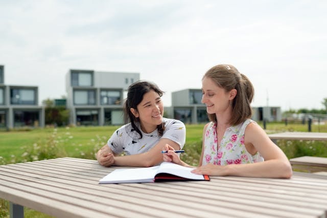 Tutot and student seated outdoors with the tutor explaining something from a notebook