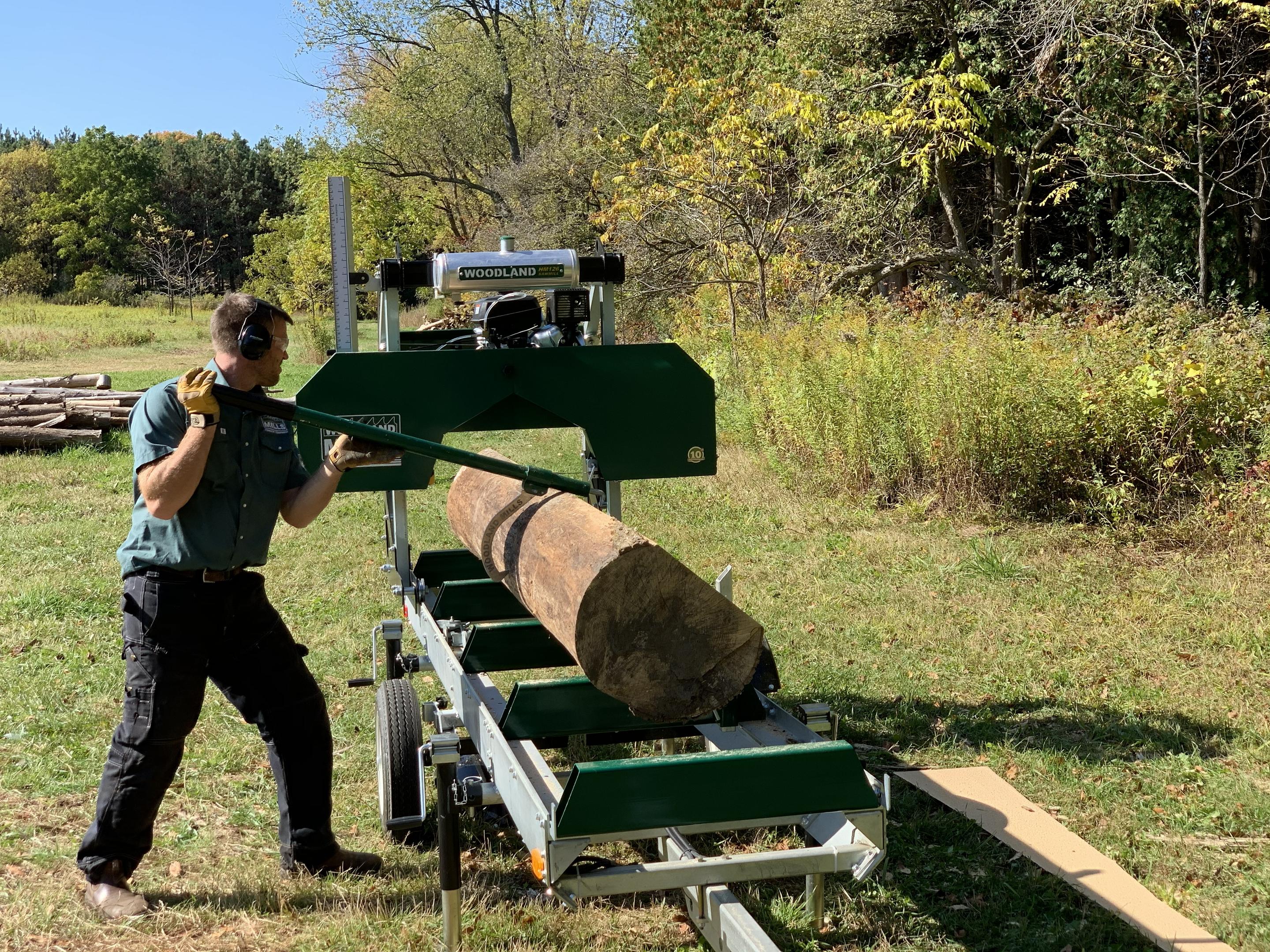 A landowner flipping a log onto the track of a Woodland Mills HM126 Portable Sawmill in a wooded area.