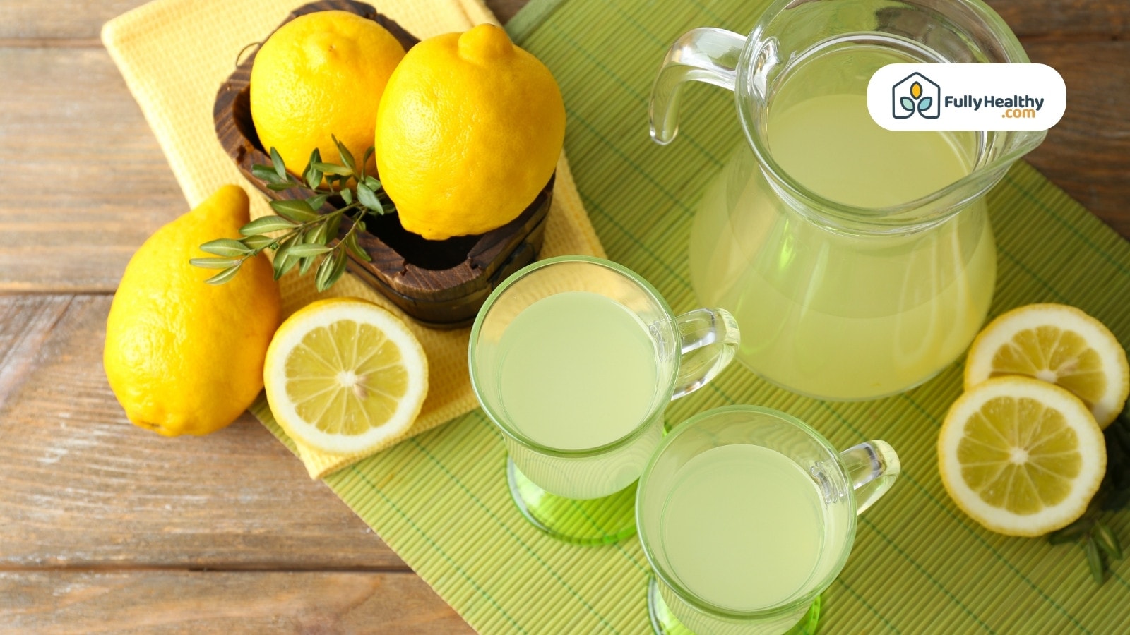 Fresh lemonade in glass pitcher and cups with whole lemons around