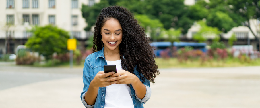 Beautiful young woman with long, dark curls smiling as she looks at her cellphone. 