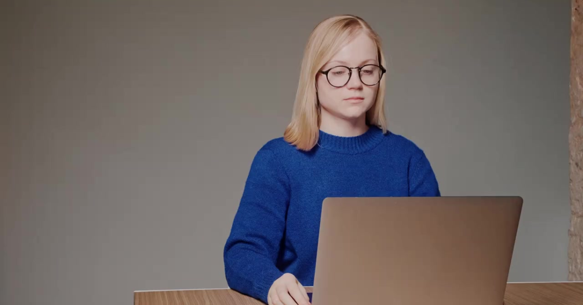 A focused woman in a blue sweater working on a laptop, efficiently managing her OnlyFans quarterly taxes.