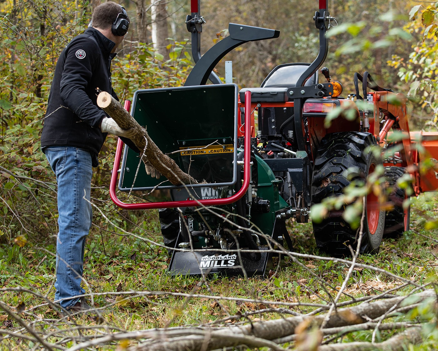An operator feeds a tree branch into the feed chute of a Woodland Mills Wood Chipper.