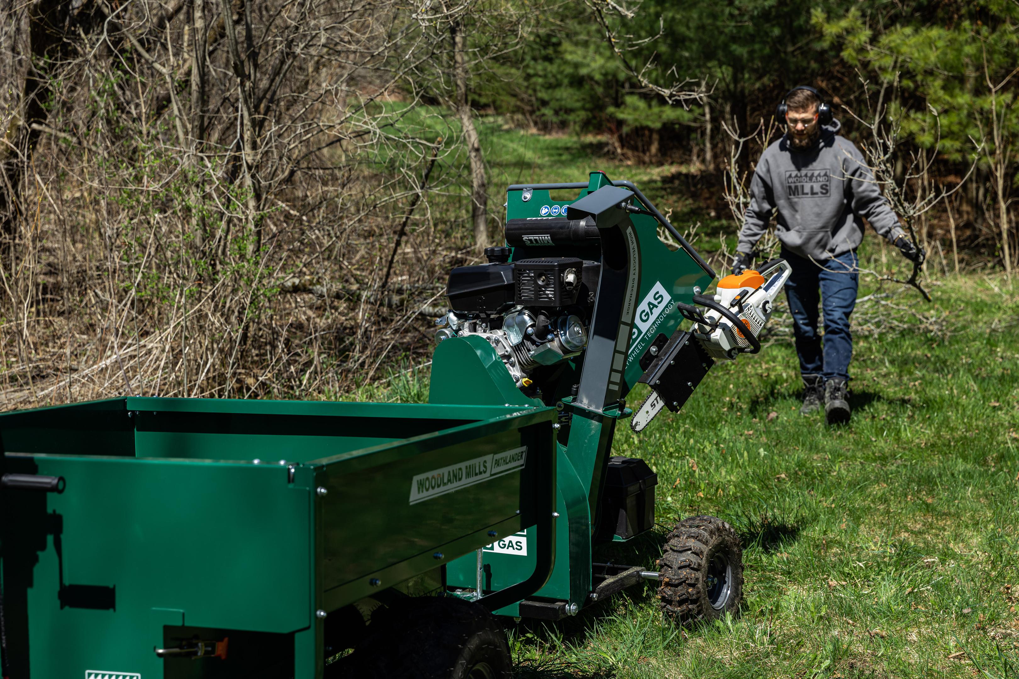 A man walking to a Woodland Mills gas-powered wood chipper attached to the back of an ATV.