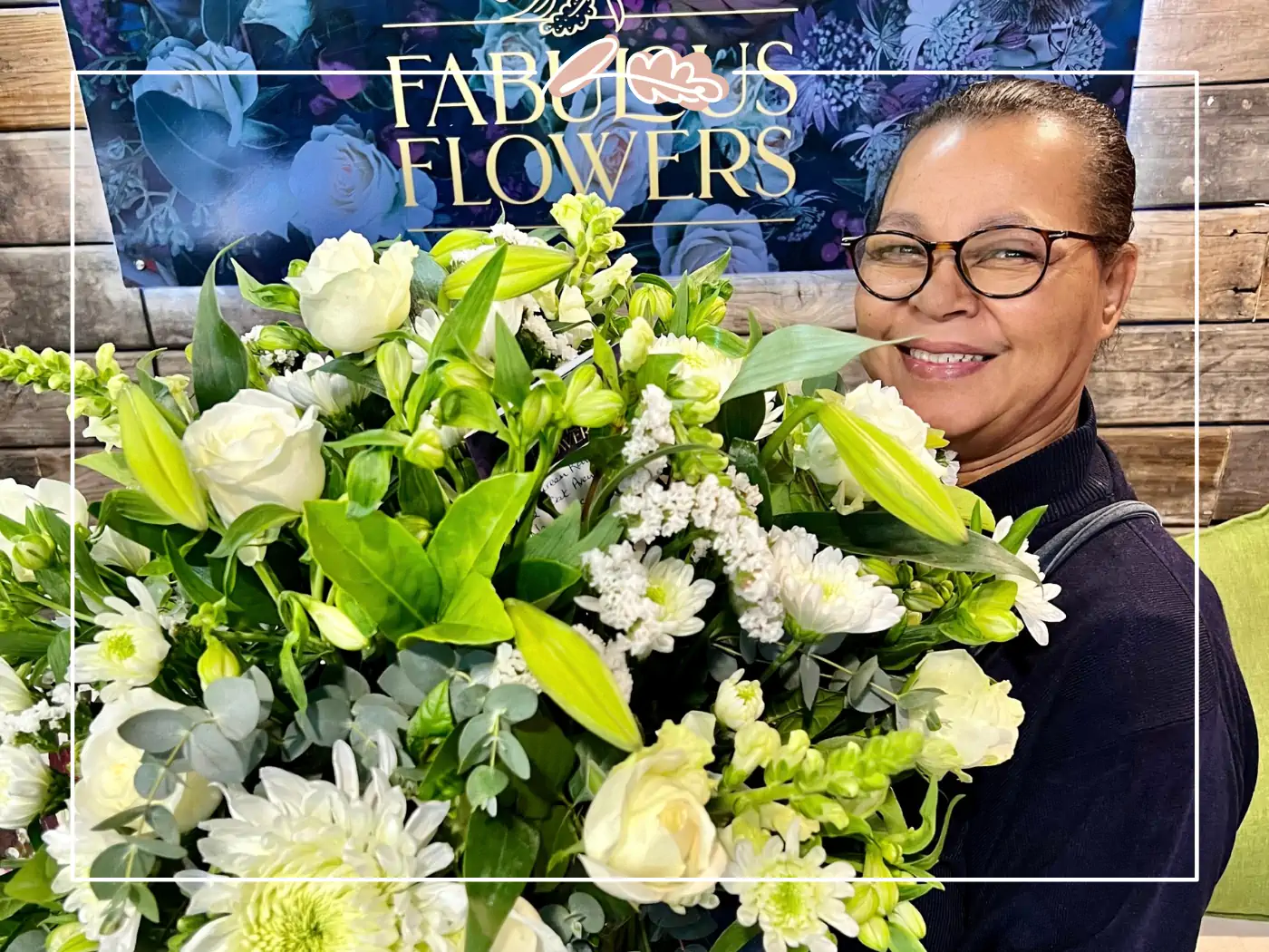 Smiling woman holding a large bouquet of white and green flowers, with Fabulous Flowers sign in the background, Fabulous Flowers and Gifts