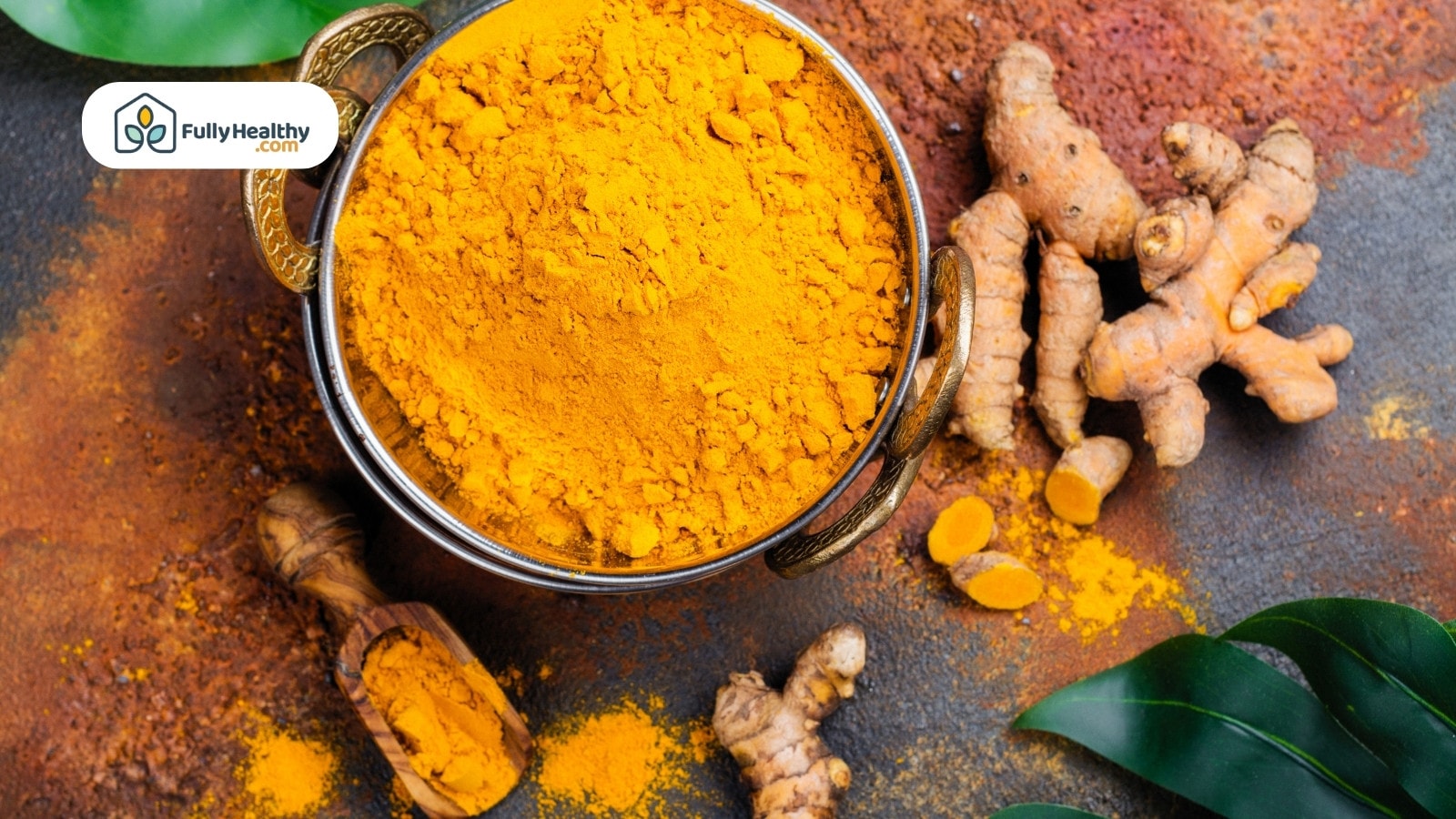 Brass bowl of turmeric powder with roots and wooden scoop beside