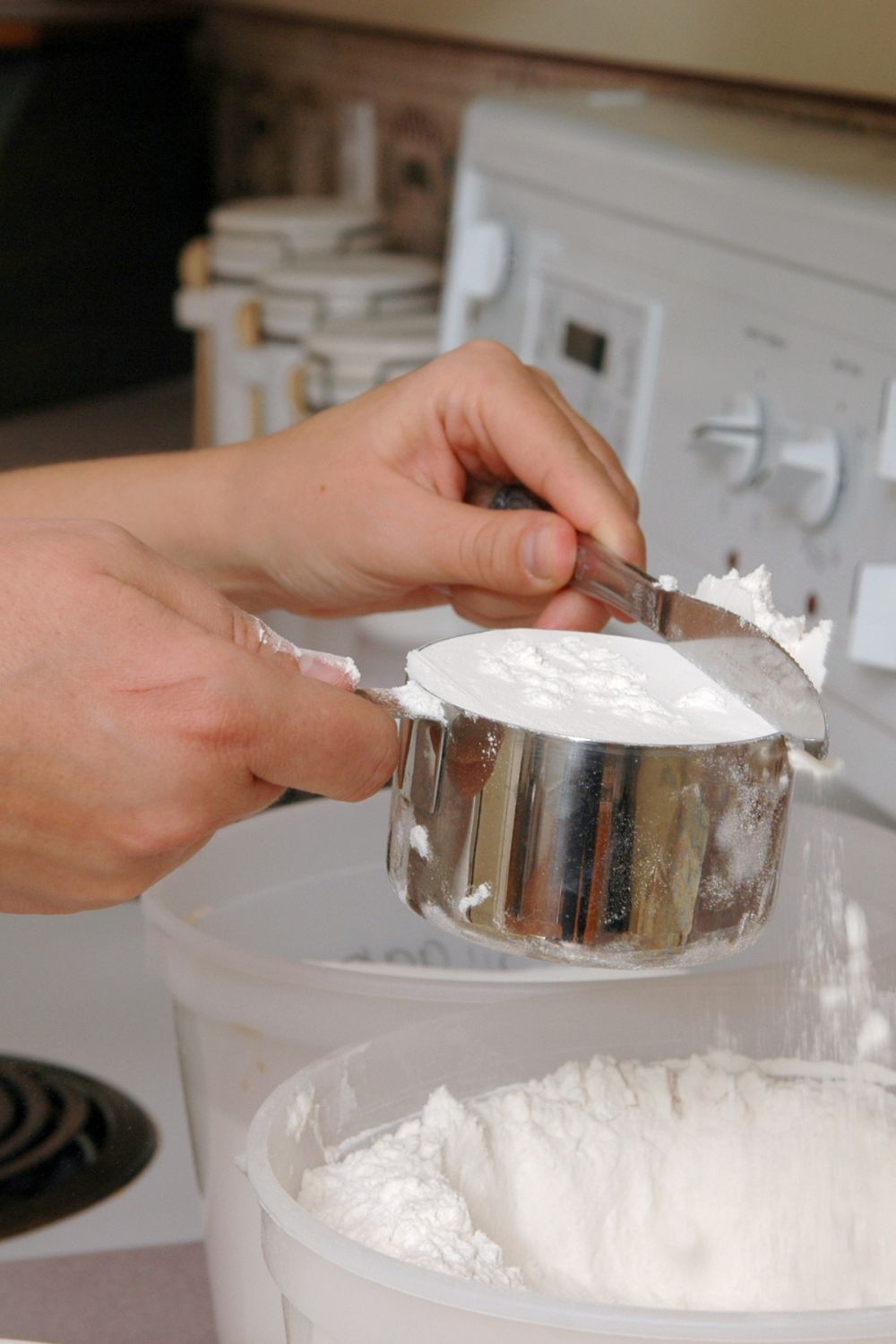 person leveling off a cup of a flour