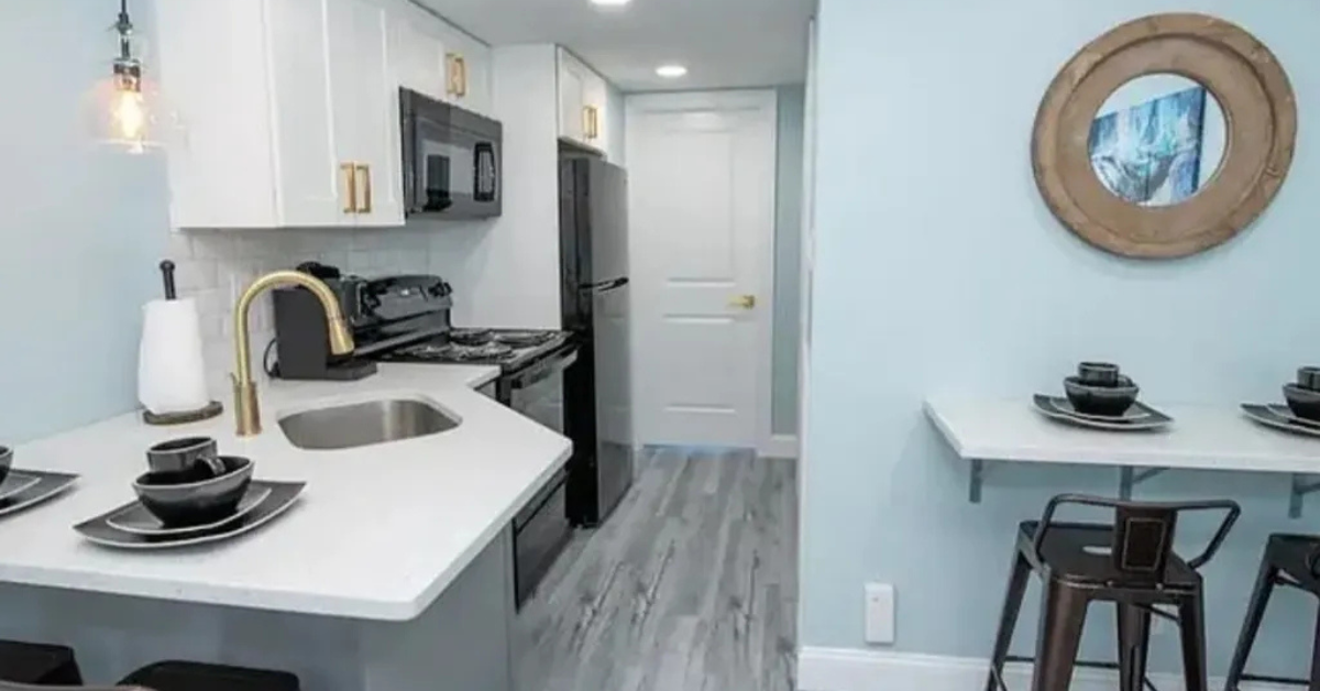 Modern furnished kitchenette at the Diplomat Wildwood with white cabinets, black appliances, and a small dining area.