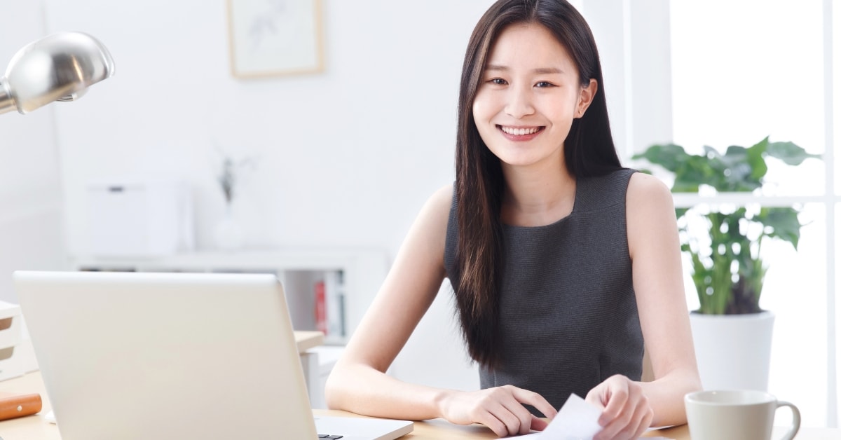  A smiling woman working at a desk with a laptop, representing expert tax help for OnlyFans creators.