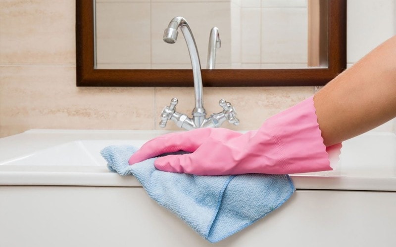 A woman scrubs a sink with a microfiber cloth.