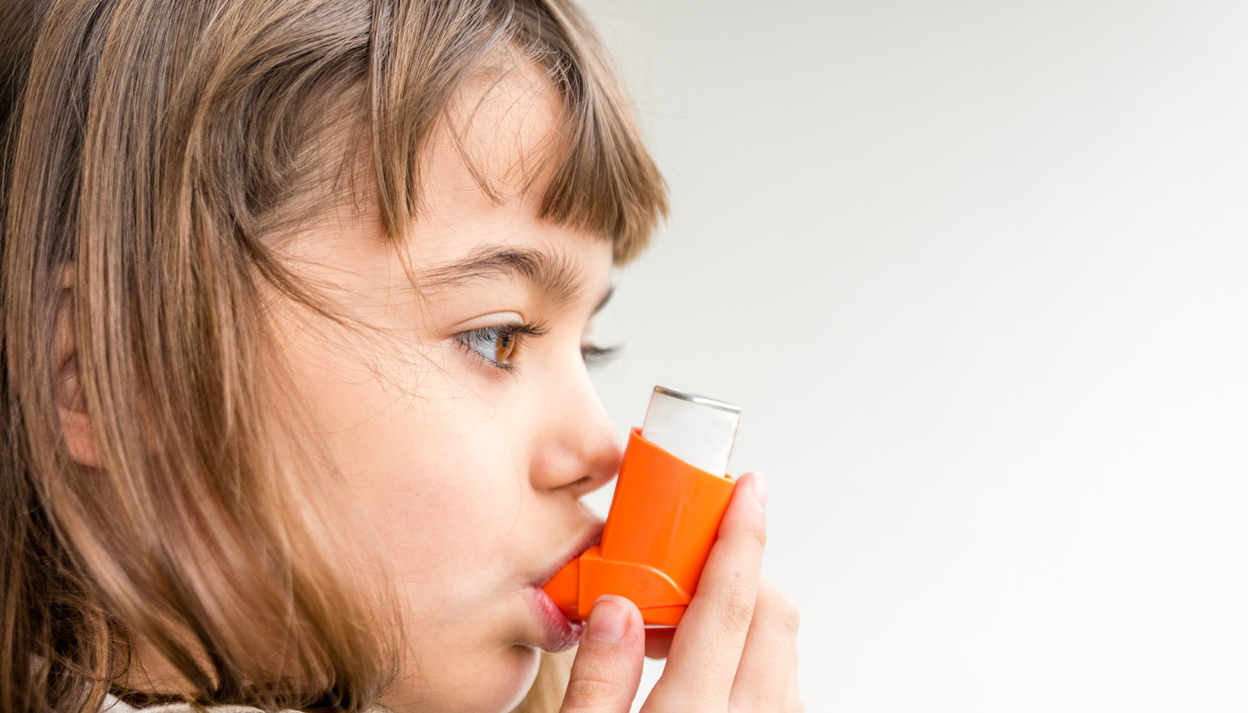 Person bruker oransje inhalator mot astma; profilvisning.