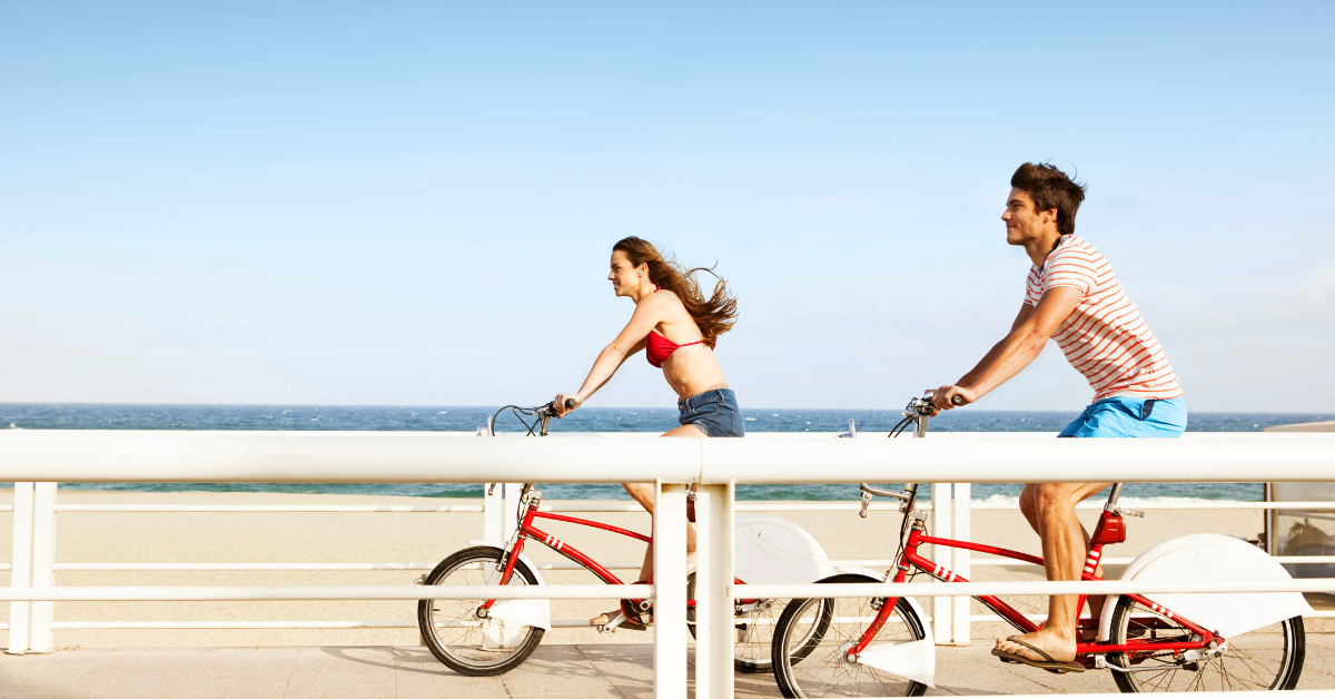 Couple riding bicycles along the Belmar boardwalk with ocean views on a clear day.