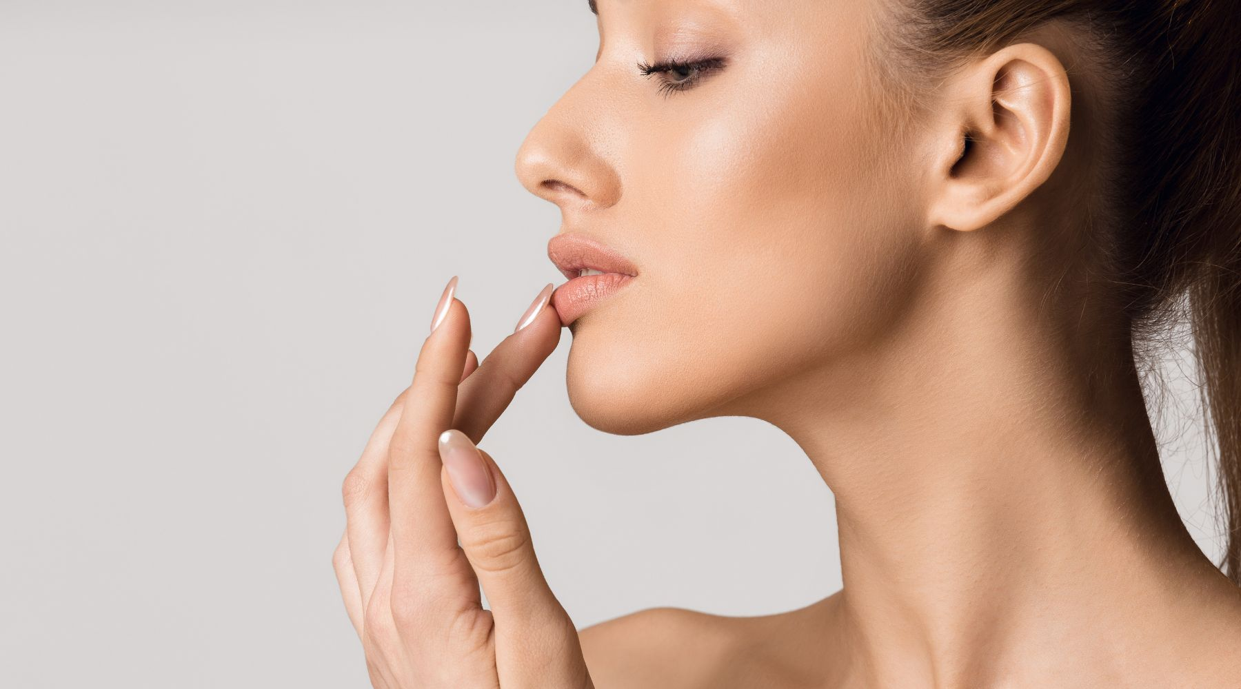 Close-up of a woman gently touching her lips, showcasing healthy skin and subtle makeup.