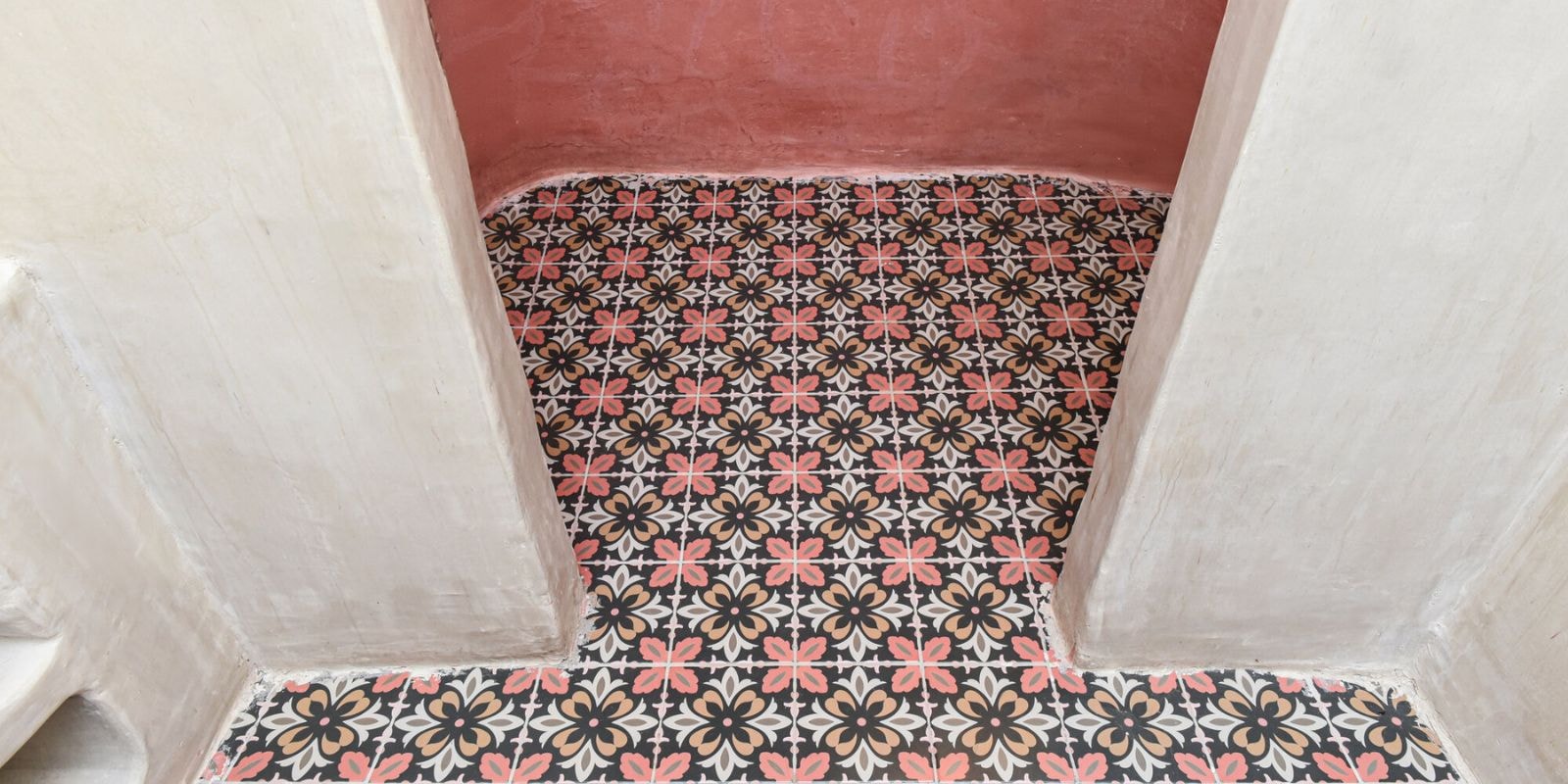 Colorful patterned floor tiles with black, coral, and beige floral motifs between cream walls.