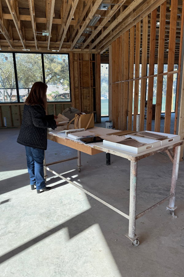 Interior designer reviewing finish samples on a temporary table inside a framed residential construction site.