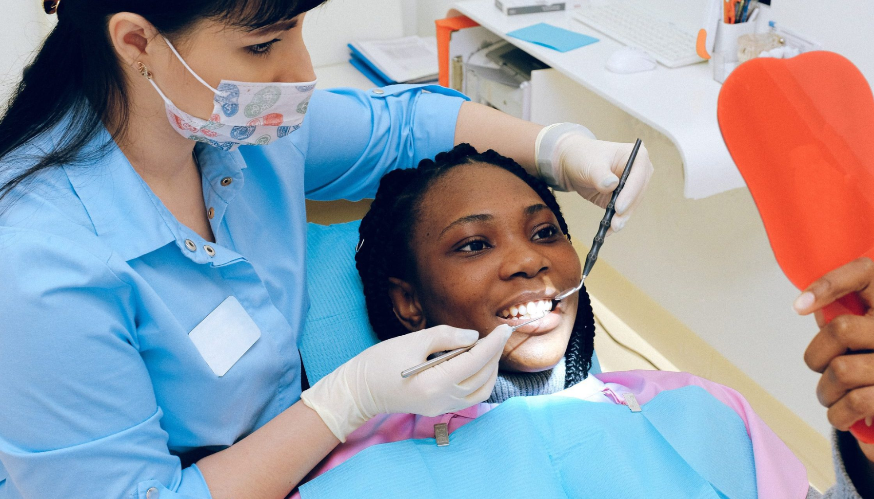 Kvinne hos tannlegen får undersøkt tennene sine mens hun smiler og holder et speil for å se resultatet selv.