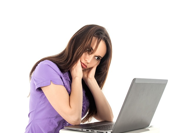 An image of a young women feeling unwell while staring at her laptop screen. 