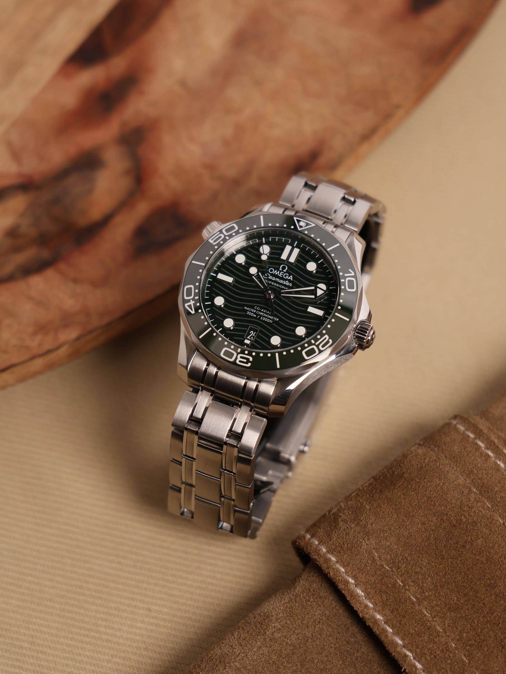 A close-up of a luxury diving watch featuring a dark ceramic bezel and a wave-patterned dial, set on a stainless steel bracelet, all against a deep blue background. This image highlights the elegance and precision of omega men's watches, particularly within the Seamaster collection.