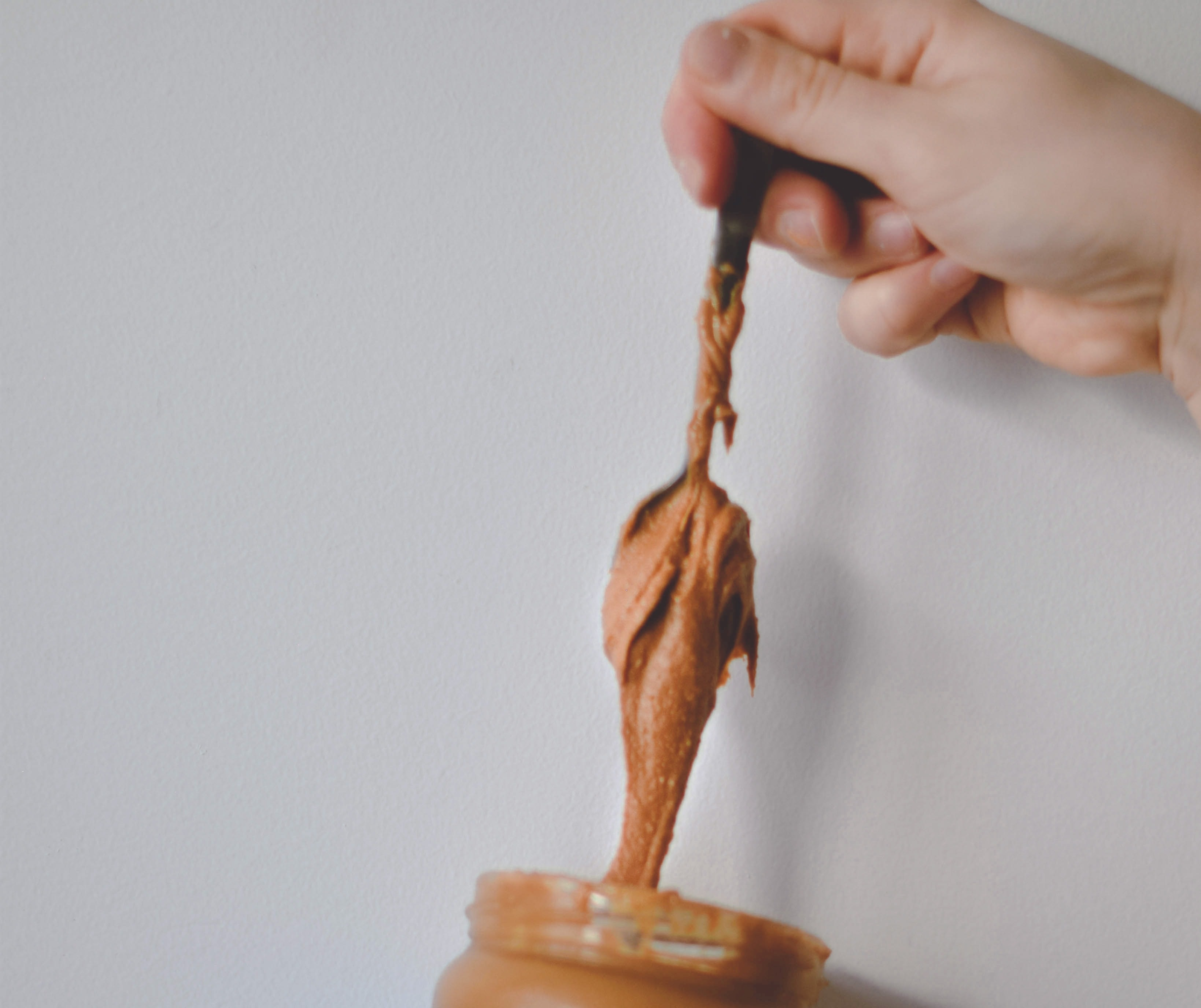 A close-up picture of a person's hand pulling out peanut butter with a spoon.
