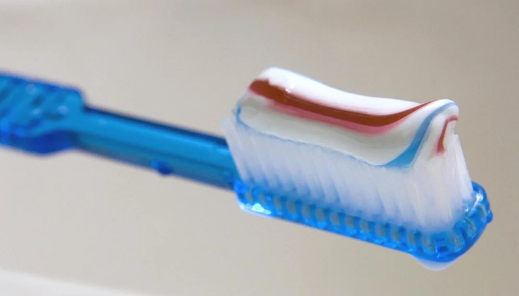 Blå tannbørste med rød, hvit og blå stripet tannkrem på børstehodet.