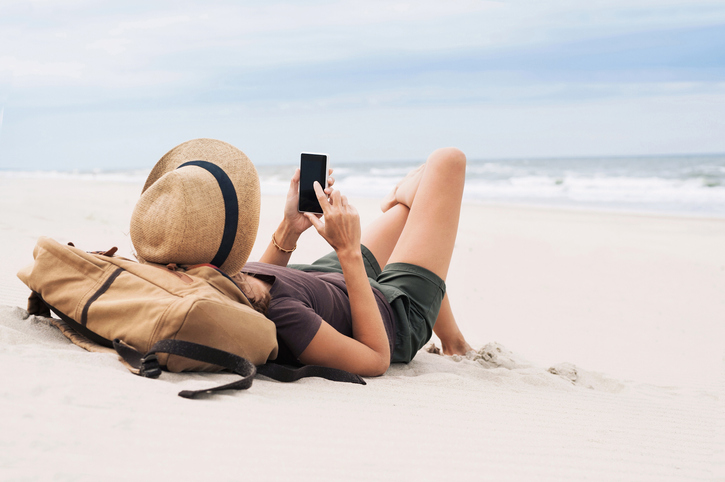 Young woman laying on the beach and looking at her phone. 