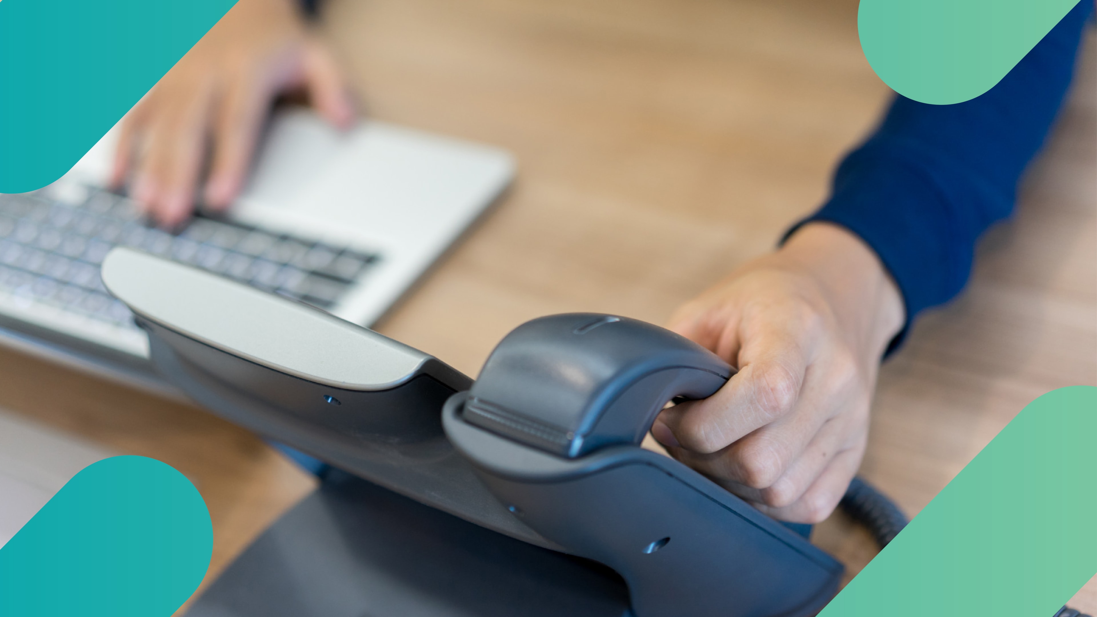 Close-up of a person picking up a desk phone handset while typing on a laptop keyboard, representing a basic business phone system.